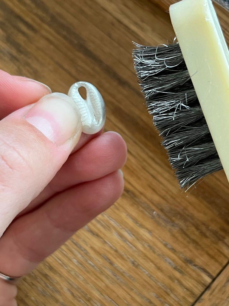 A wire brush brushing a silver clay piece. 
