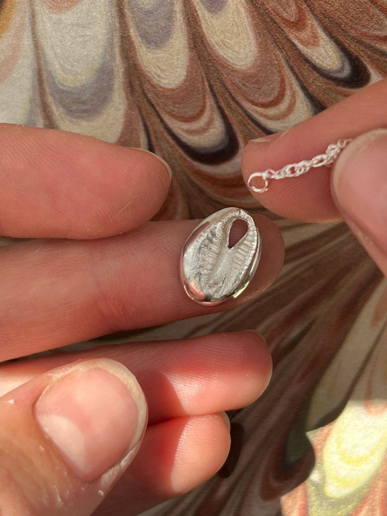 A silver chain about to be threaded through the hole of a silver clay piece. 