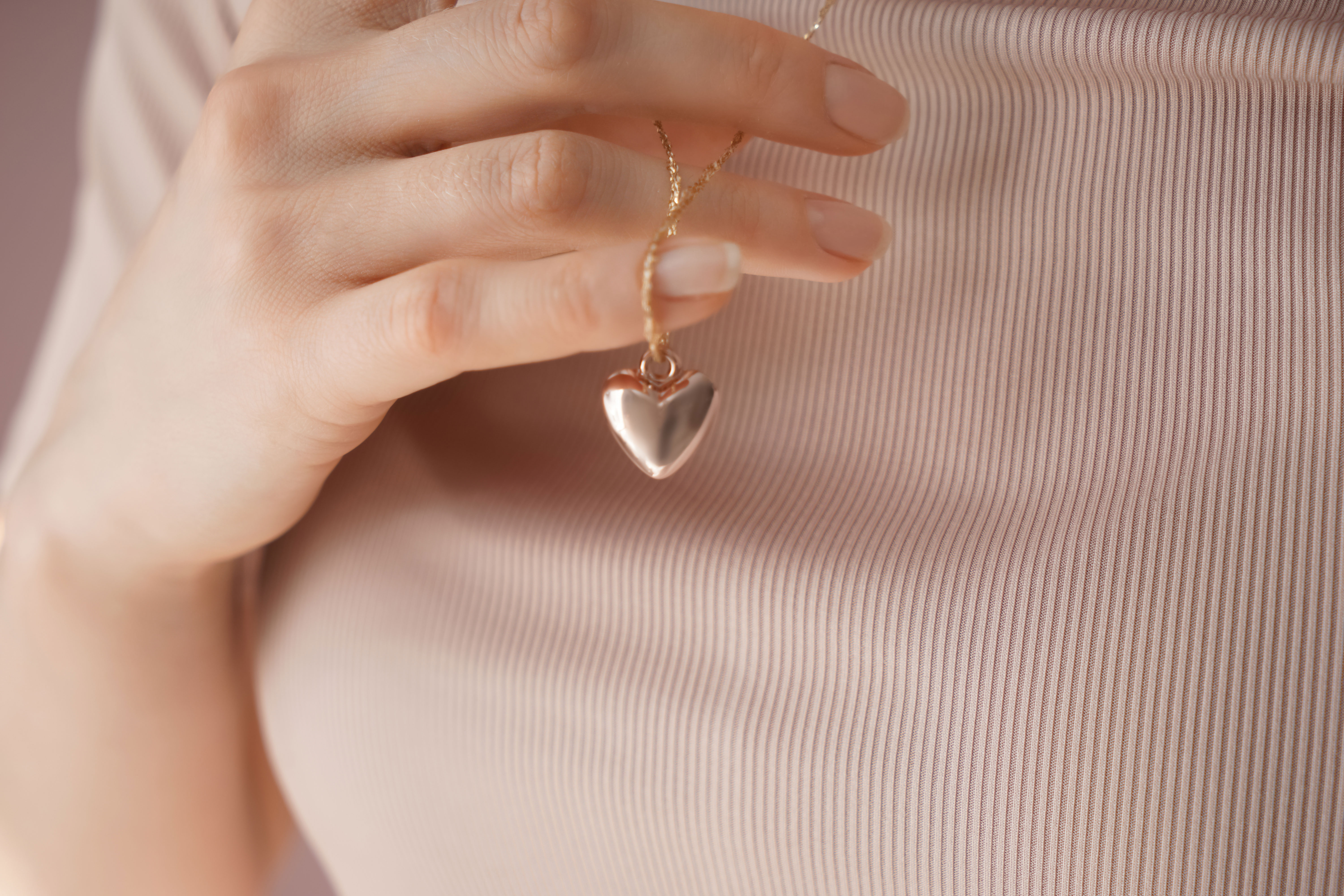 Someone holding a heart shaped pendant which hangs on a chain around their neck.