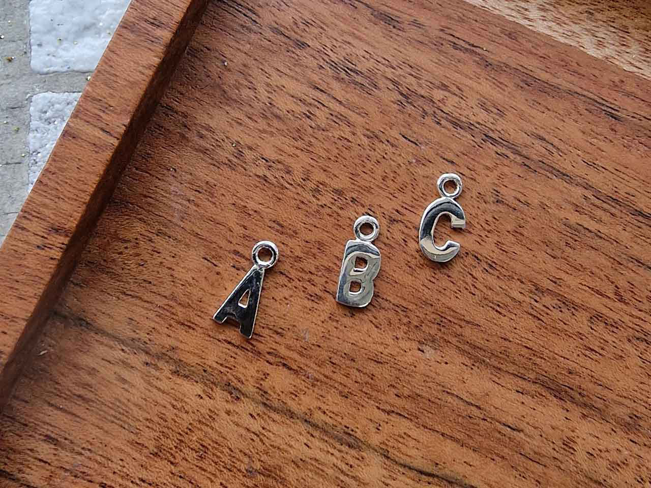 Letter pendants A, B and C, shown on a workbench, as one of the autumn 2023 jewellery trends. 