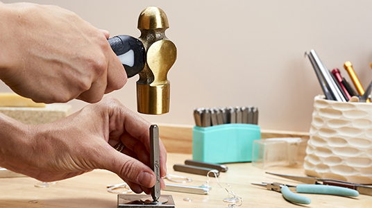 jeweller using a hammer on a metal blank